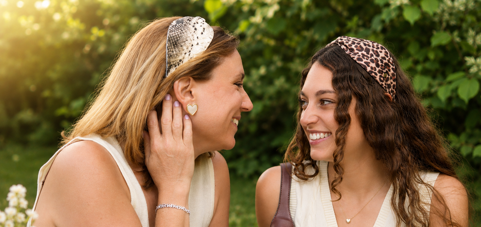 Deux femmes souriantes avec des bandeaux colorés, entourées de feuillage.